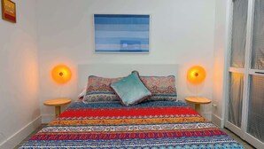 A bed with patterned bedding, two bedside lamps, a wall-mounted picture, and a window with blinds. - After Hours - Wilton Drive and Jacuzzi (Wilton Manors)