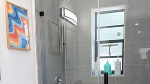 A modern bathroom with a glass-enclosed shower, a white toilet, and a sink with a countertop. - After Hours - Wilton Drive and Jacuzzi (Wilton Manors)