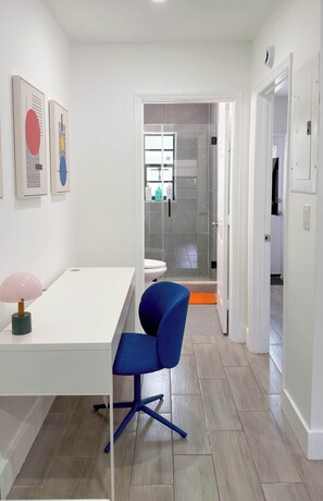 A modern bathroom with a glass shower enclosure, a white toilet, and a blue chair in a hallway with a white floor and walls. - After Hours - Wilton Drive and Jacuzzi (Wilton Manors)