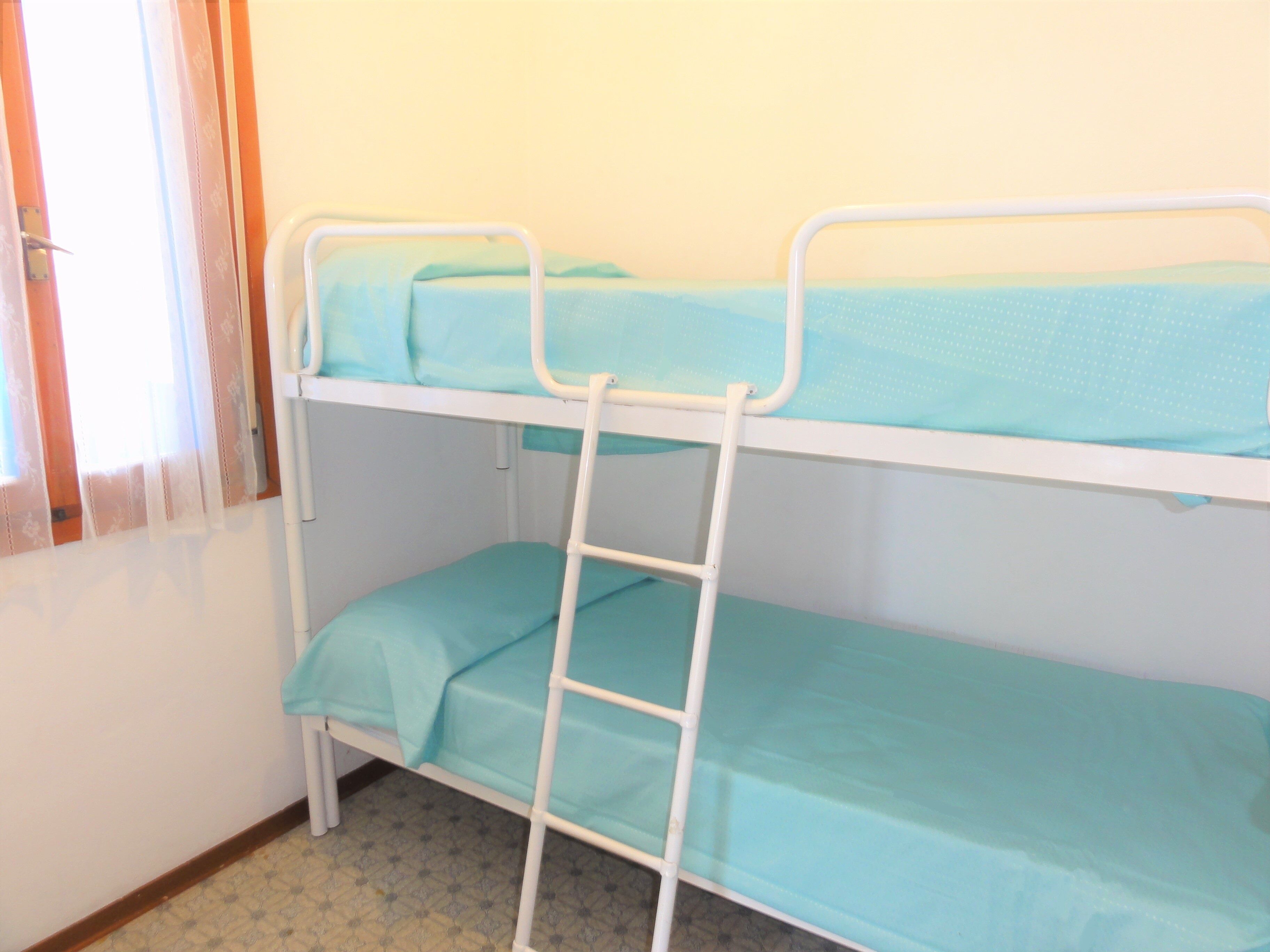 A bunk bed with a ladder, a window with curtains, and a patterned floor.