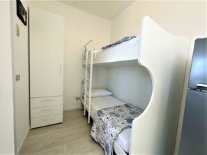 A small, compact room with a bunk bed, a wardrobe with multiple drawers, and a refrigerator. - Bibione Apartment With sea View Terrace (San Michele al Tagliamento)