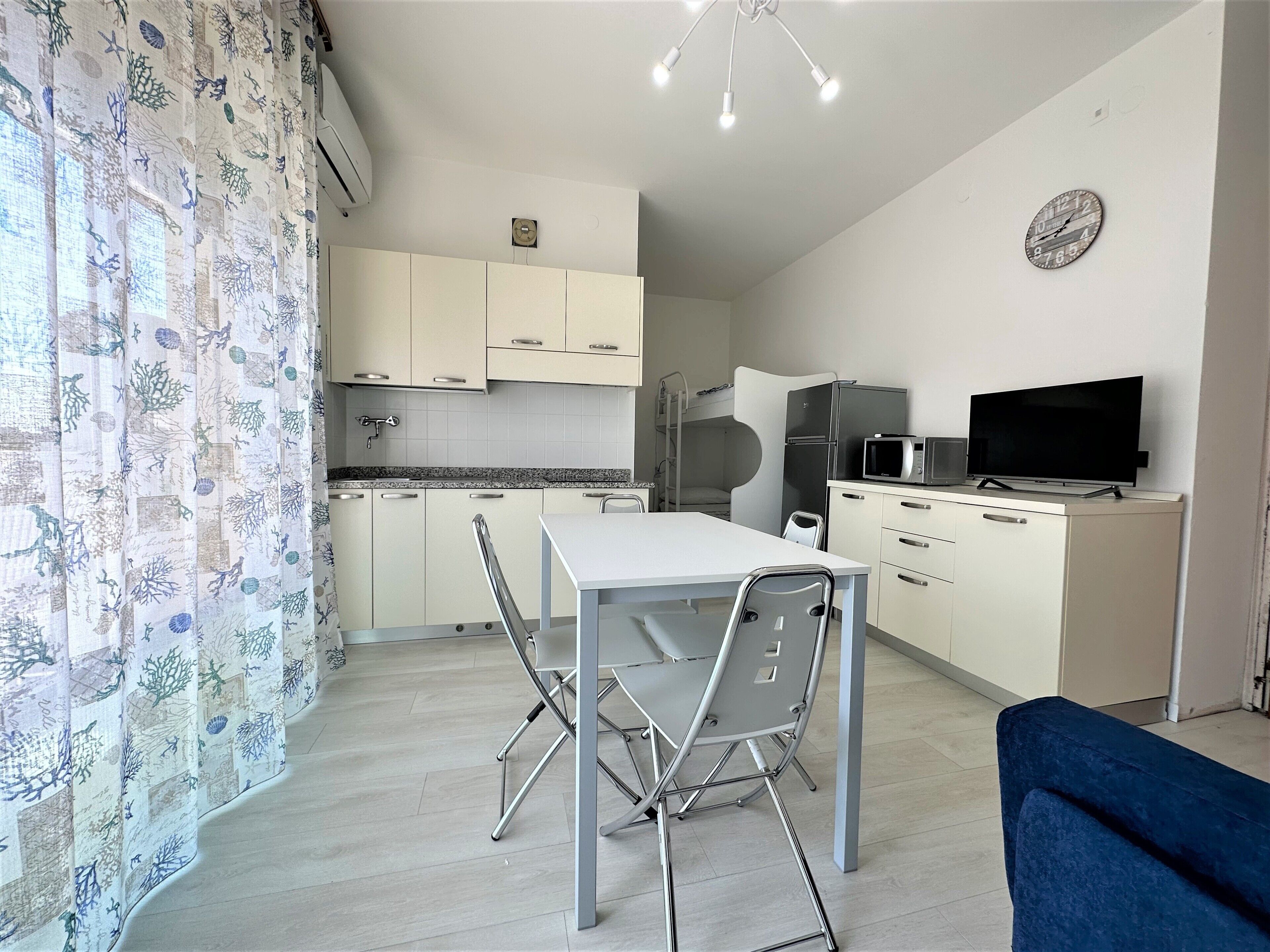 A compact kitchen with a dining table and chairs, a microwave, a refrigerator, and a television.