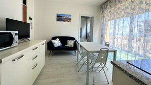 Una cucina moderna con zona pranzo, forno a microonde, TV a schermo piatto e vista all'esterno attraverso ampie finestre.