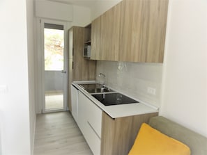 Une cuisine de taille réduite, dotée de meubles en bois, d’un évier en acier inoxydable et d’un plan de travail blanc.