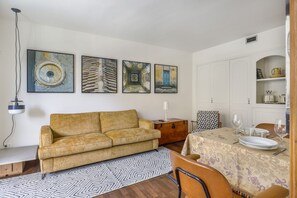 A living room with a sofa, a dining table set for two, and four artworks on the wall.