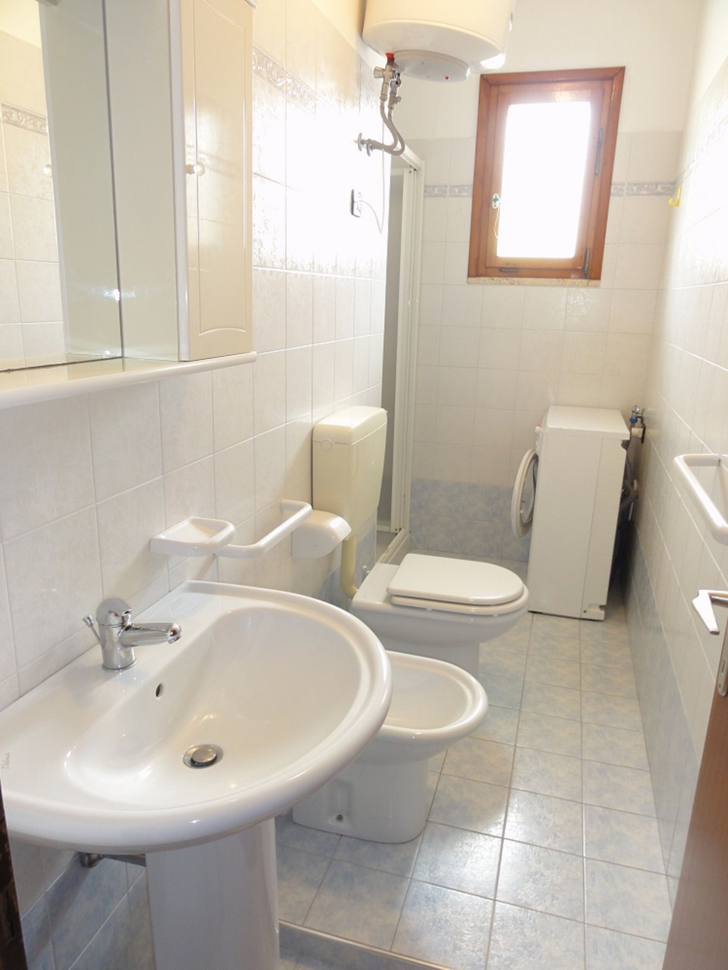 A compact bathroom with a sink, two toilets, and a shower.
