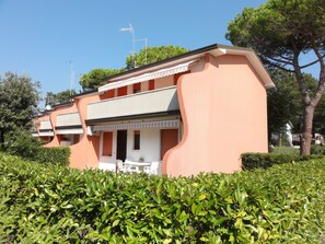 Un edificio a due piani con tetto piatto, un balcone con ringhiere bianche e un tavolino con sedie all'esterno.