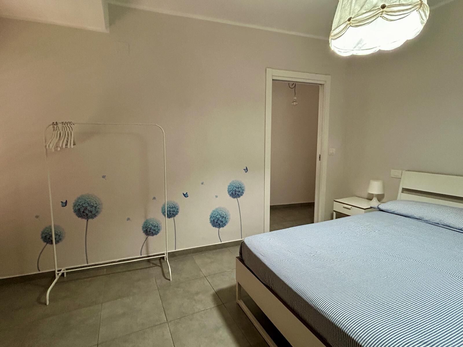A bedroom with a bed, a nightstand, a lamp, and a wall with a floral pattern.