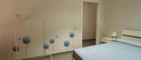A bedroom with a bed, a nightstand, a lamp, and a wall with a floral pattern.