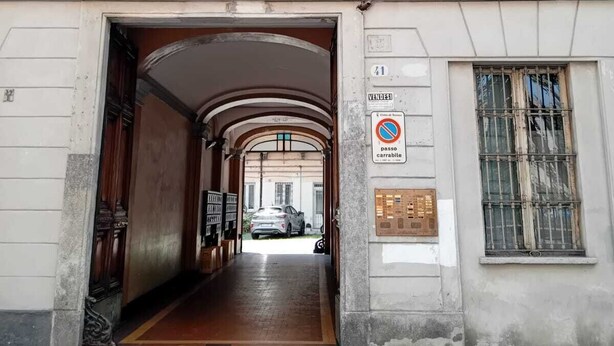Ingresso di un edificio con una porta di legno, un segnale che indica divieto di parcheggio e un veicolo parcheggiato all'interno.