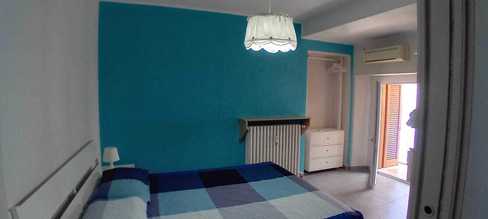 A bedroom with a bed, a radiator, a wardrobe, and a door leading to a balcony.