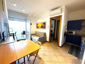 A compact living space with a dining area, a sofa, a kitchen with blue cabinets, and an air conditioning unit.
