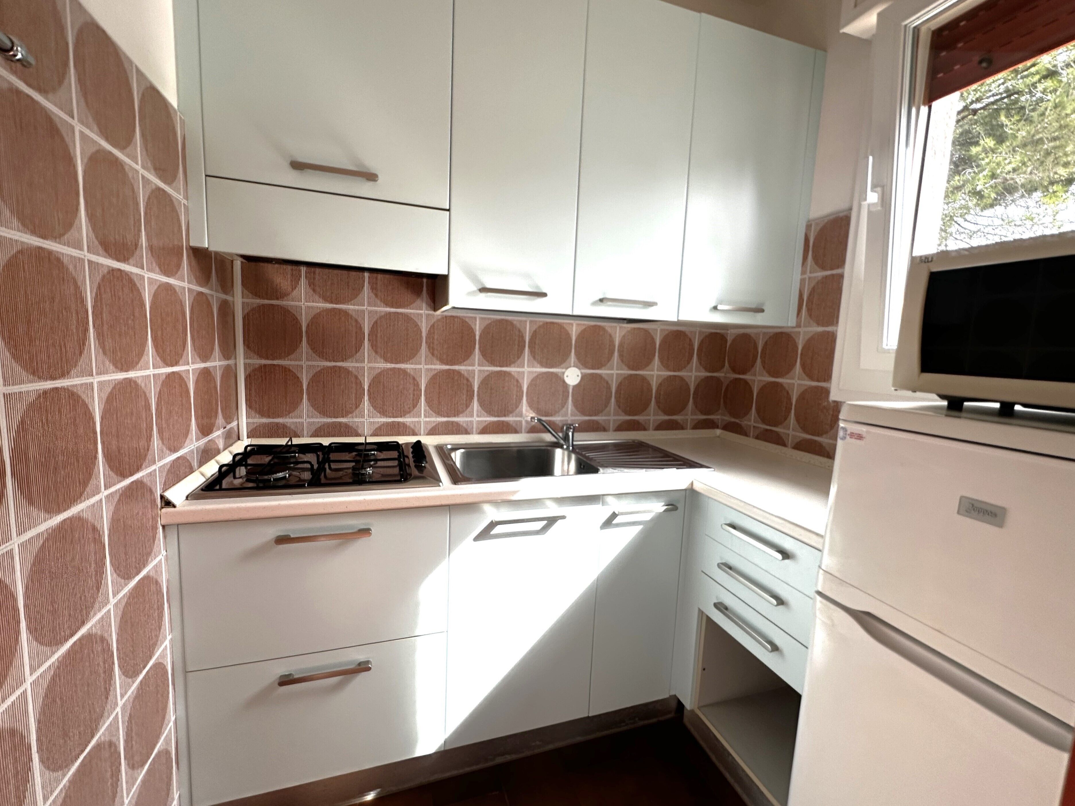 A compact kitchen with white cabinets, a gas stove, a sink, and a built-in microwave.