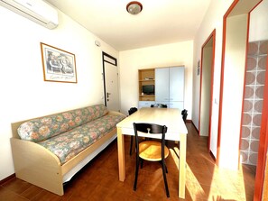 A room with a sofa, a dining table with chairs, a TV on a shelf, and a door with a mirror. - Lovely Flat With Pool-beahost (San Michele al Tagliamento)
