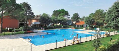 A swimming pool surrounded by a fence, with people swimming and walking around.