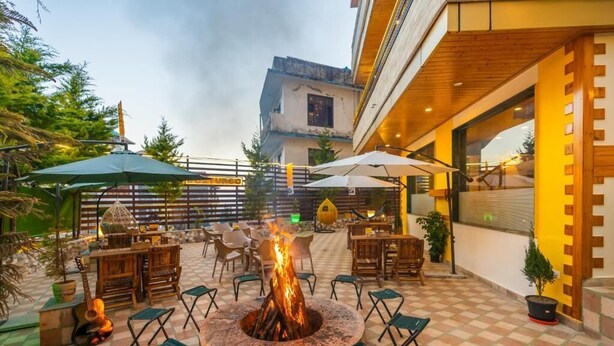 Une terrasse extérieure dotée d’un foyer central, entourée de chaises et de tables pliantes, et agrémentée de parasols pour créer de l’ombre.