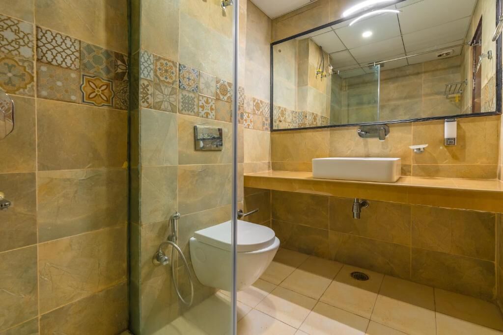 A bathroom with a glass shower enclosure, a white toilet, and a beige tiled wall with a decorative tile border.