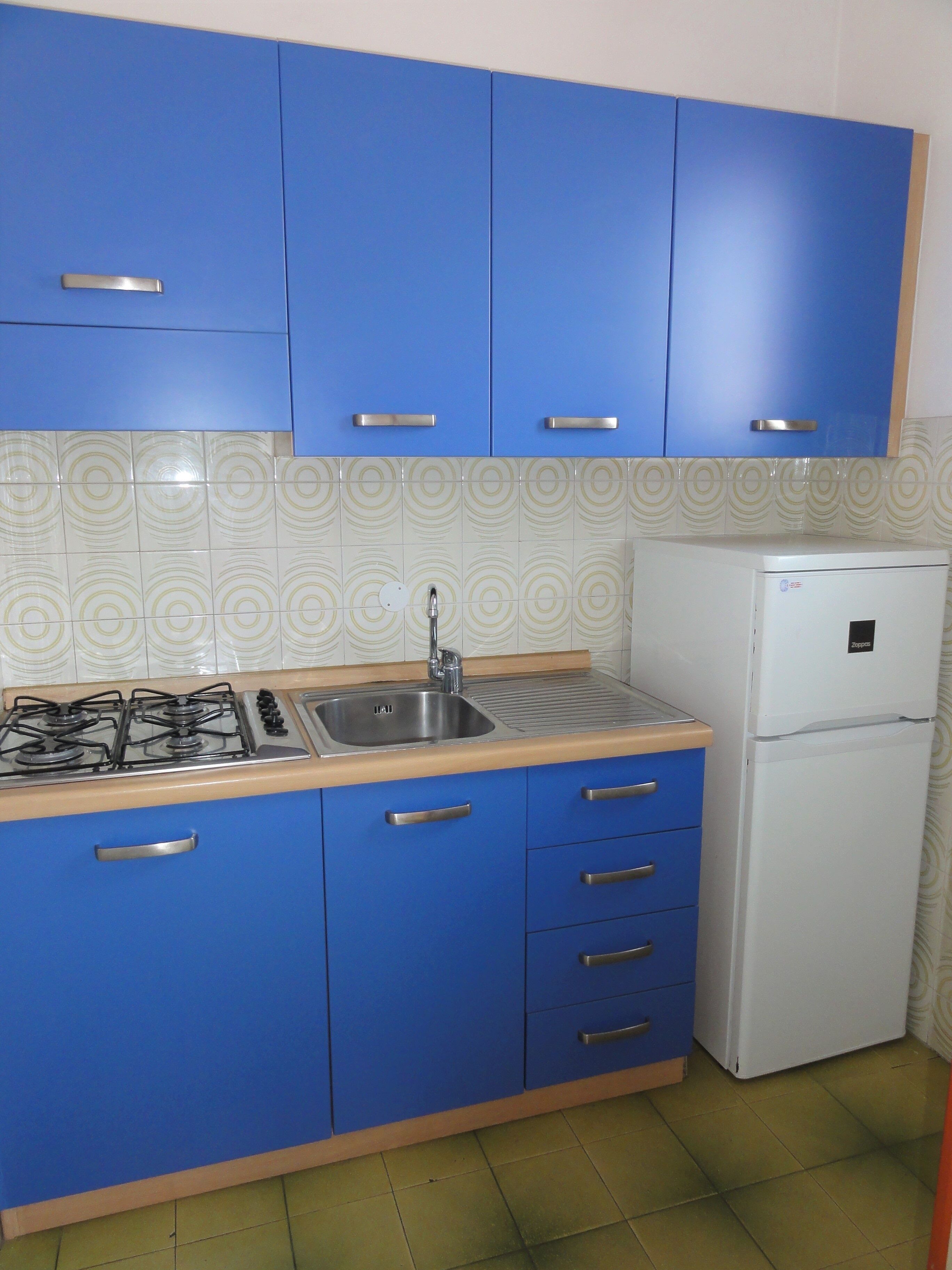A kitchen with blue cabinets, a gas stove, a sink, and a white refrigerator.