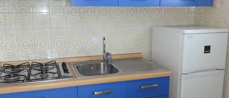 A kitchen with blue cabinets, a gas stove, a sink, and a white refrigerator.