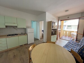 A compact kitchen with a dining area, a sofa, and a sliding glass door leading to an outdoor patio. - Comfortable Apartment Near the Beach (San Michele al Tagliamento)