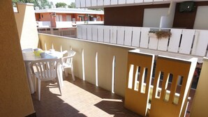 Un balcon avec une table et des chaises, une clôture en bois et un bâtiment en arrière-plan.