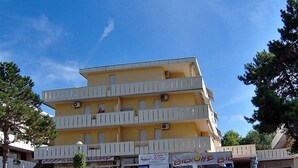 Un immeuble à plusieurs étages doté de balcons, d’une enseigne et d’un espace verdoyant à l’avant.