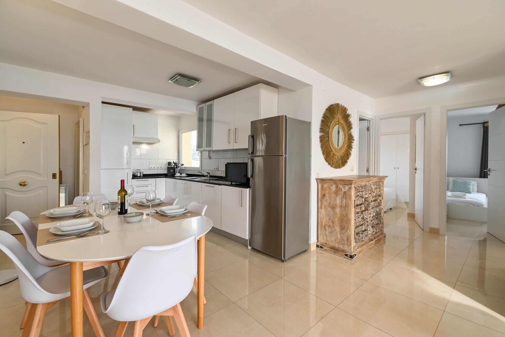 A modern kitchen with white cabinets, a stainless steel refrigerator, and a dining area with a table and chairs.