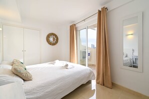 A hotel room with a bed, a round mirror, a window with curtains, and a view of the city.