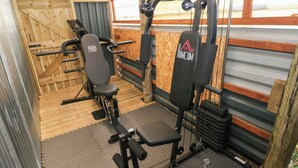 Ett gym med olika typer av träningsutrustning, inklusive en bänkpress, en benpress och en kabelmaskin.