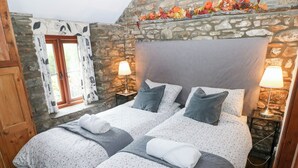 En dubbelsäng med blommigt sänglinne, två sänglampor och en vägg i sten som bakgrund.