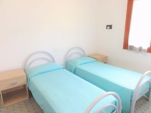 Une petite pièce simple, avec deux lits simples, une table de chevet en bois et une petite table.