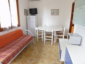A small, well-lit room with a sofa, a table with chairs, a television, a refrigerator, and a microwave. - Colorful Flat in a Villa With Garden (San Michele al Tagliamento)