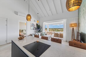 Une cuisine moderne dotée d’un grand îlot central, d’un coin repas avec des chaises et d’une vue sur un quartier résidentiel par les fenêtres.