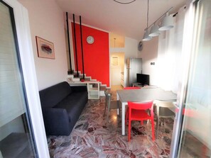 A modern living space with a black sofa, red chairs, a marble-patterned floor, a staircase with red accents, and a dining area with a table and chairs. - Comfy Villa With Garden (San Michele al Tagliamento)