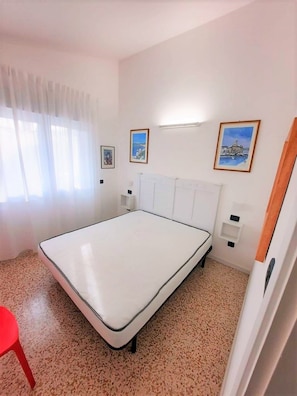 A bedroom with a single bed, white walls, and a red chair. There are two framed pictures on the wall. - Comfy Villa With Garden (San Michele al Tagliamento)