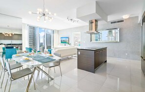 A modern kitchen with a central island, large windows, and a dining area with a table set for two. - Vibrant Brickell 2BR | Riverwalk & City Access (Miami)