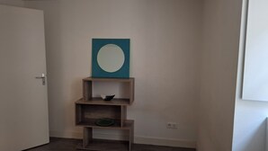 A corner of a room with a white door, a wooden shelf unit with a teal artwork above it, and a small green decorative item on the bottom shelf.