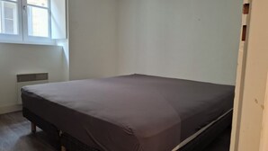 A small, single-bed room with a plain white wall, a window with closed blinds, and a radiator.