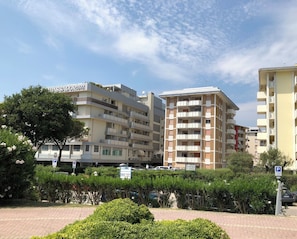 A multi-story residential building with balconies, a parking sign, and a tree in the foreground.