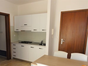 A kitchen with white cabinets, a gas stove, and a wooden door.