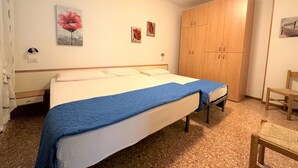 A bedroom with a bed, a wooden wardrobe, and a chair. - Bibione Apartment Close to Promenade (San Michele al Tagliamento)
