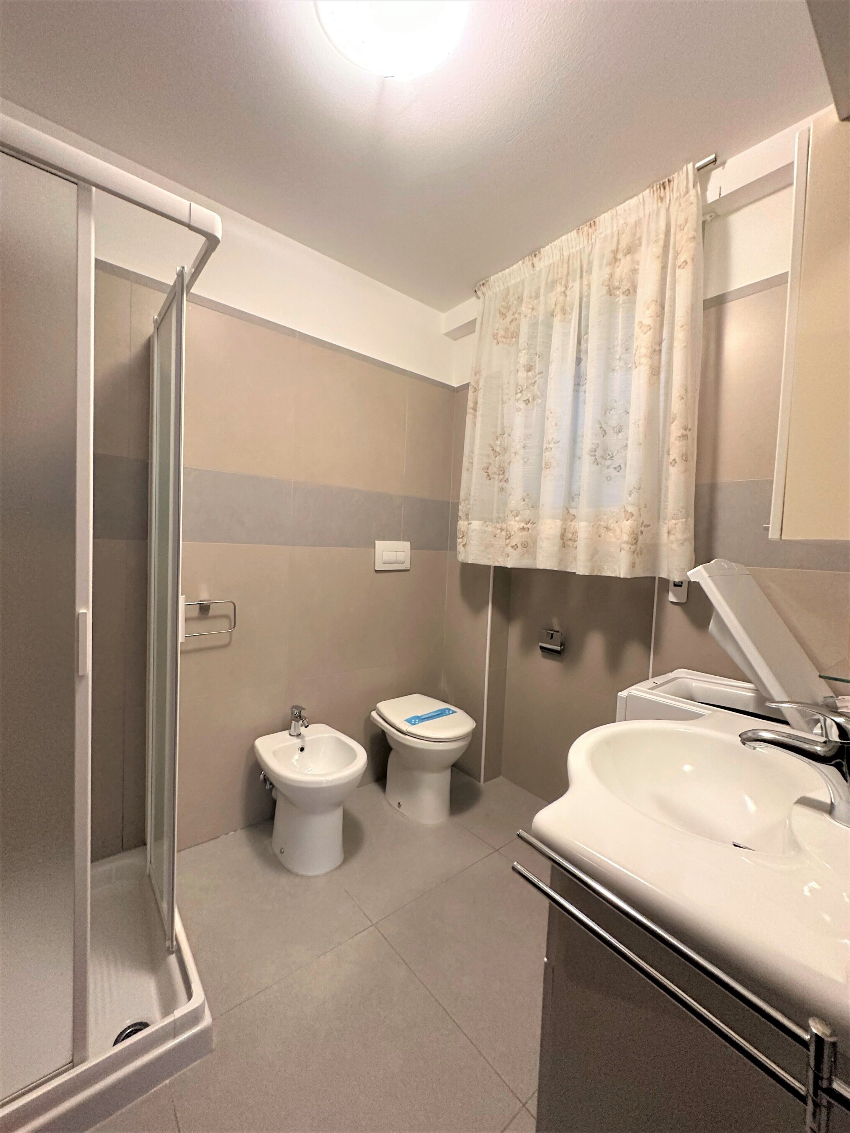 A bathroom with a shower, toilet, bidet, and sink.