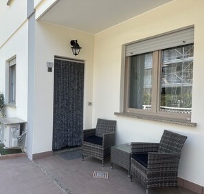 A balcony with wicker chairs, a window with blinds, and an air conditioning unit. - Bibione Apartment Close to Promenade (San Michele al Tagliamento)