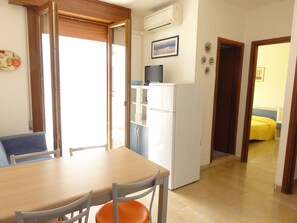 Une cuisine compacte équipée d’un réfrigérateur, d’une table à manger avec des chaises et d’une porte coulissante donnant sur une autre pièce.