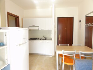 Eine kompakte Küche mit weißen Schränken, einem Gasherd und einem Essbereich mit Holztisch und Stühlen.