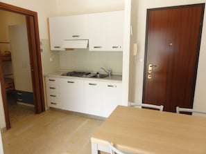Una cocina con gabinetes blancos, estufa a gas, un lavamanos y una puerta de madera.