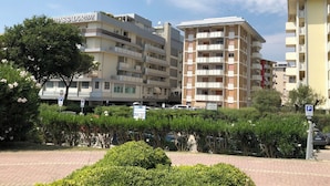 A multi-story residential building with balconies, a parking sign, and a tree in the foreground. - Coastal Apartment With Terrace (San Michele al Tagliamento)