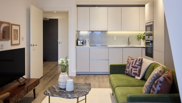 A modern living room with a green sofa, a coffee table, and a TV. Adjacent is a kitchen with white cabinets and a microwave. - Streatham Hill Modern Flat with Balcony (London)