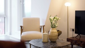 A modern living room with a round table, a white chair, a vase with flowers, and a lamp. - Streatham Hill Modern Flat with Balcony (London)