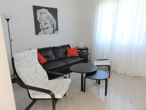 A modern living room with a black leather sofa, a white armchair, a small round table, and a floor lamp. - Bibione Pineda Villa With Garden and BBQ (San Michele al Tagliamento)